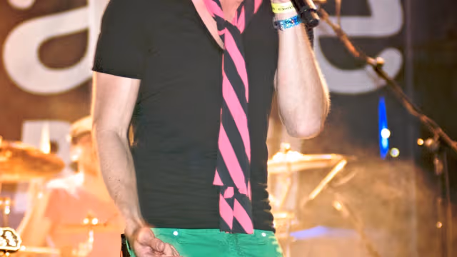 Fiuk cantando em show, com chapéu e calça verde