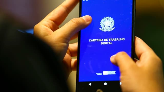 Mãos de uma pessoa segurando um celular com o aplicativo da Carteira de Trabalho Digital aberto na tela