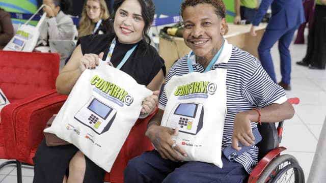 Evento do TSE com participantes segurando sacolas da campanha de combate à desinformação, com bandeira do Brasil ao fundo