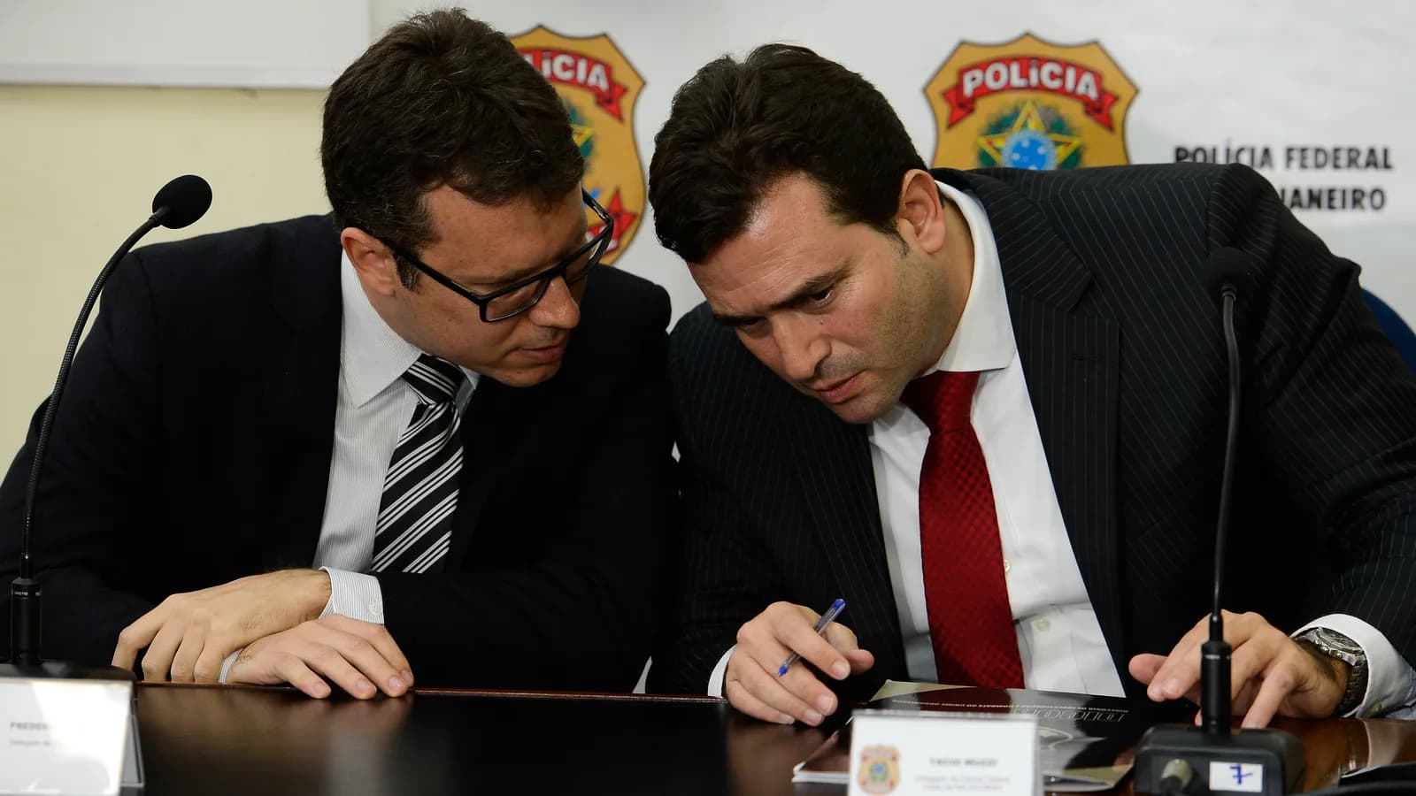 Delegados da Polícia Federal concedem coletiva de imprensa em frente a painel com o brasão da corporação