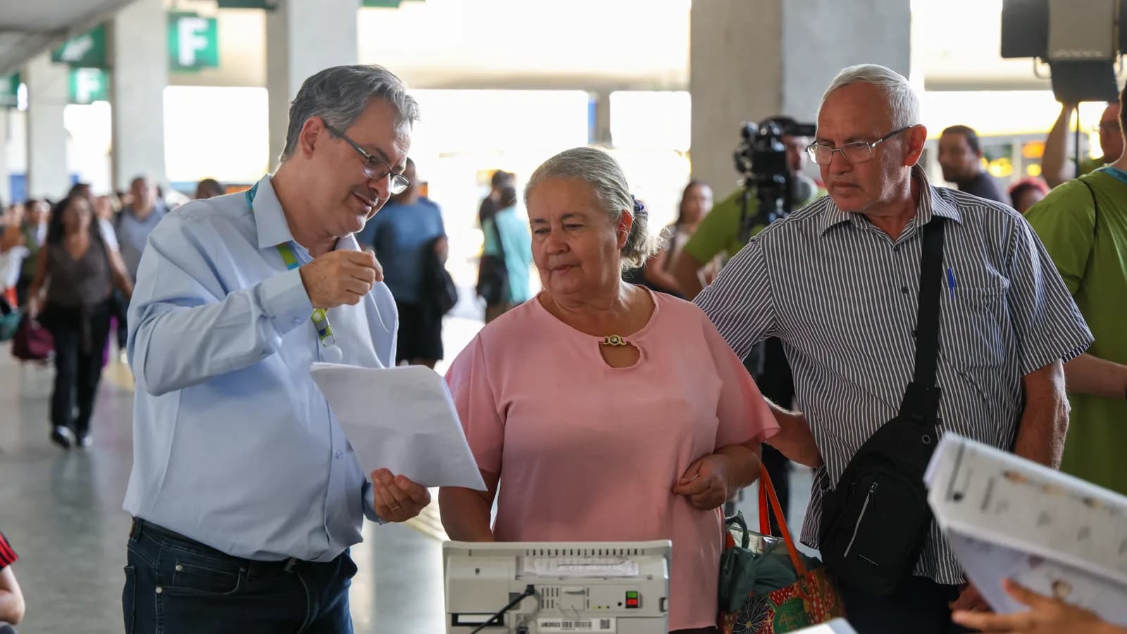 Servidor do TSE mostra documento a eleitores ao lado de urna eletrônica em ação educativa na rodoviária de Brasília