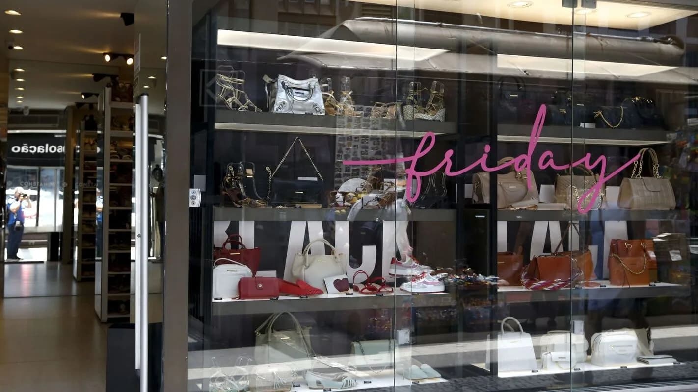 Vitrine de loja de bolsos e calçados decorada com letreiro de Black Friday, com pessoas refletidas no vidro