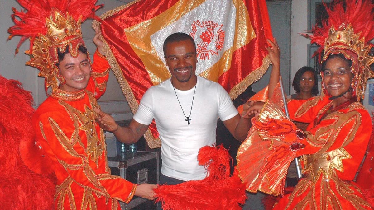 O cantor Alexandre Pires sorri ao lado de integrantes de escola de samba em evento