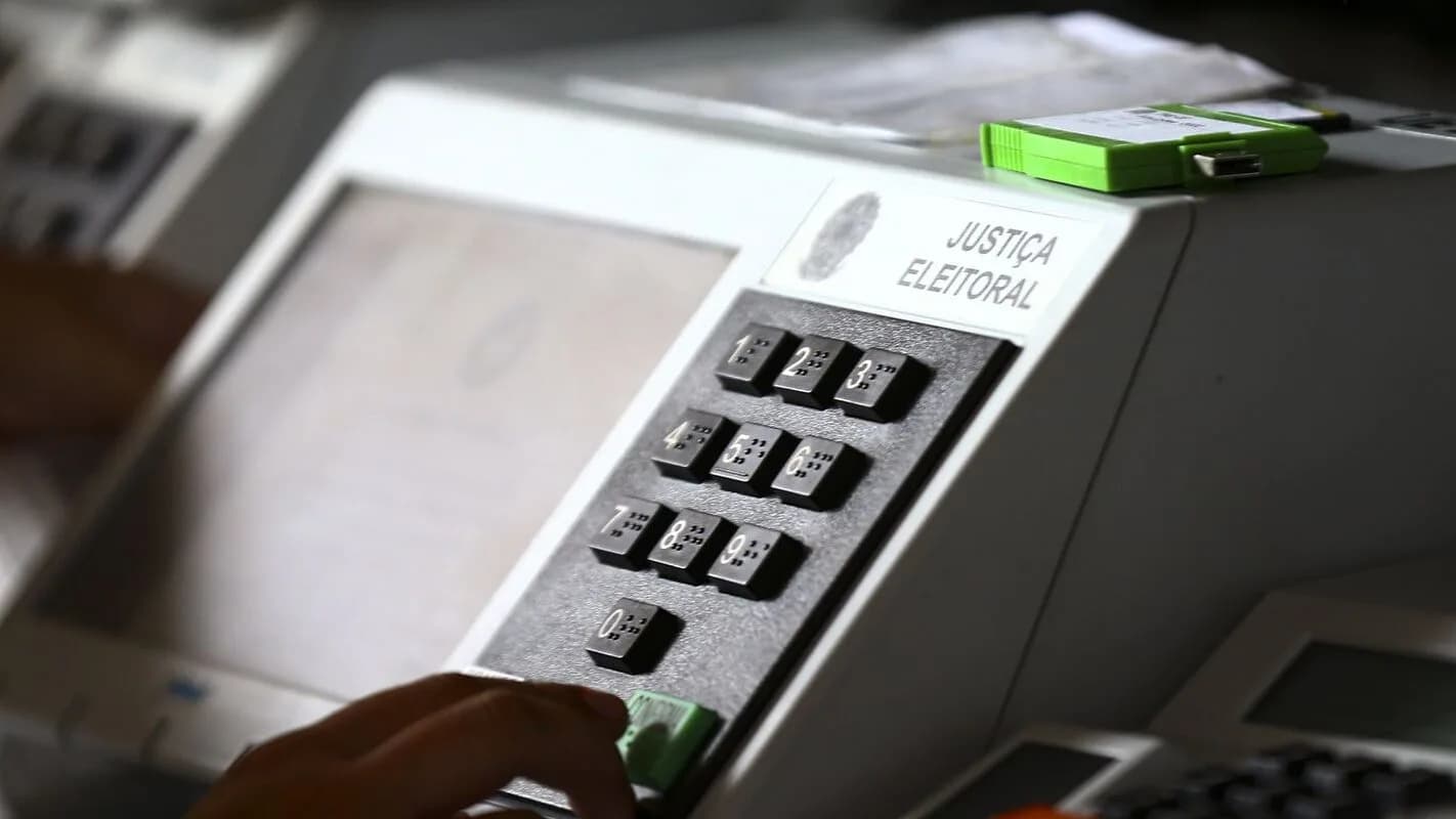 Close de urna eletrônica brasileira durante teste de segurança, com mãos manuseando o teclado