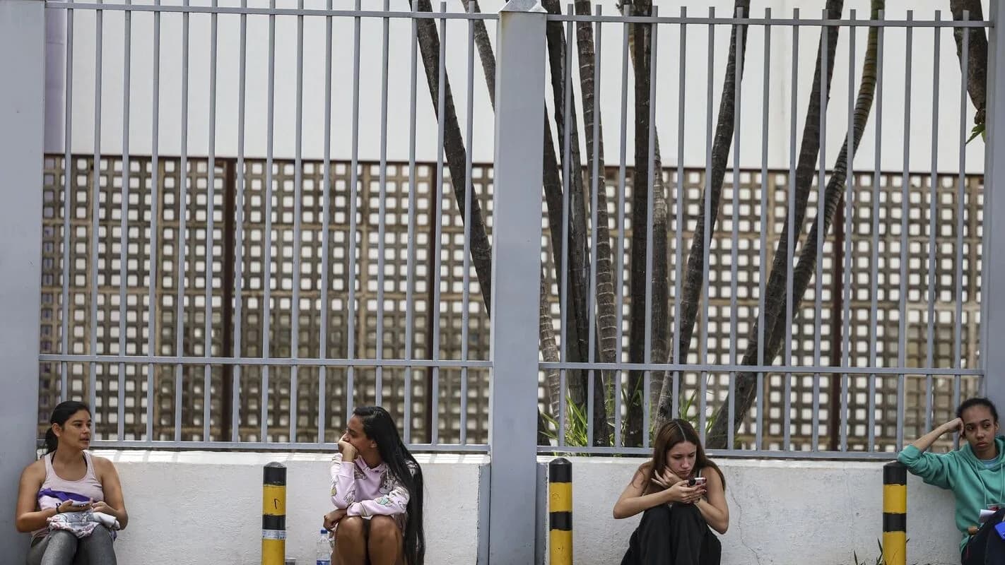 Candidatos sentados em banco de concreto aguardam do lado de fora de local de prova