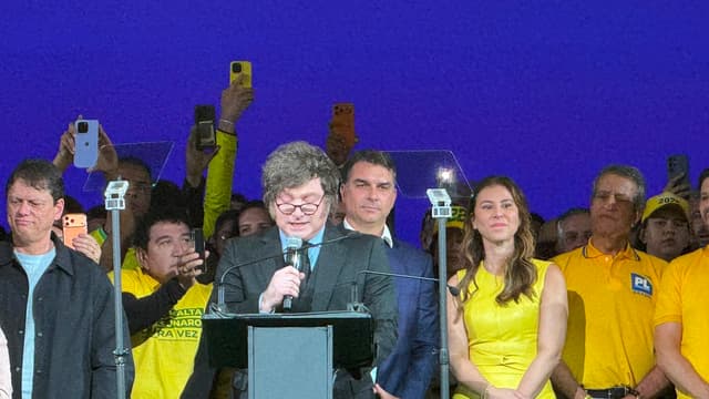 O presidente da Argentina, Javier Milei, discursa ao microfone no palco da convenção do PL, em São Paulo, cercado por apoiadores de camisa amarela que filmam com celulares