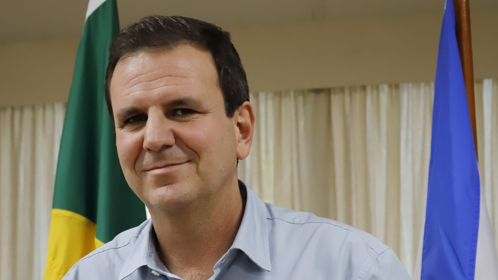 Eduardo Paes, prefeito do Rio de Janeiro, posa com as bandeiras do Brasil e da cidade ao fundo