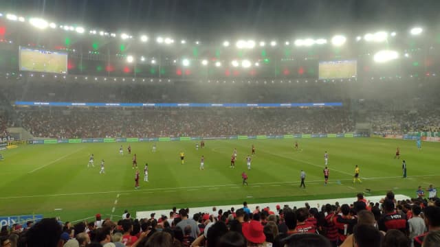 Torcida acompanha jogo do Flamengo no Maracanã, com o gramado iluminado ao fundo