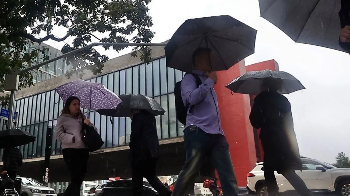 Pedestres andam sob chuva com guarda-chuvas na Avenida Paulista, em São Paulo, com o MASP ao fundo