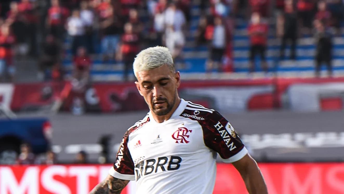 Arrascaeta, com a camisa branca do Flamengo, conduz a bola em campo