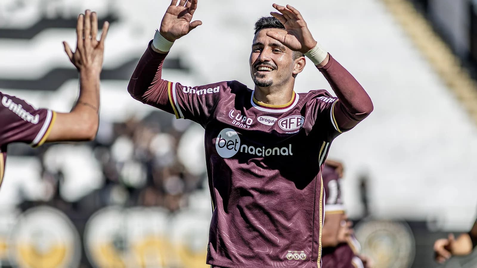 Jogador da Ferroviária comemora gol em partida, vestindo uniforme grená do clube