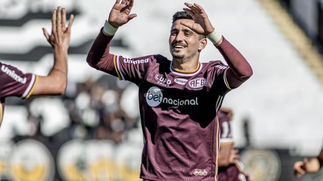 Jogador da Ferroviária comemora gol em partida, vestindo uniforme grená do clube