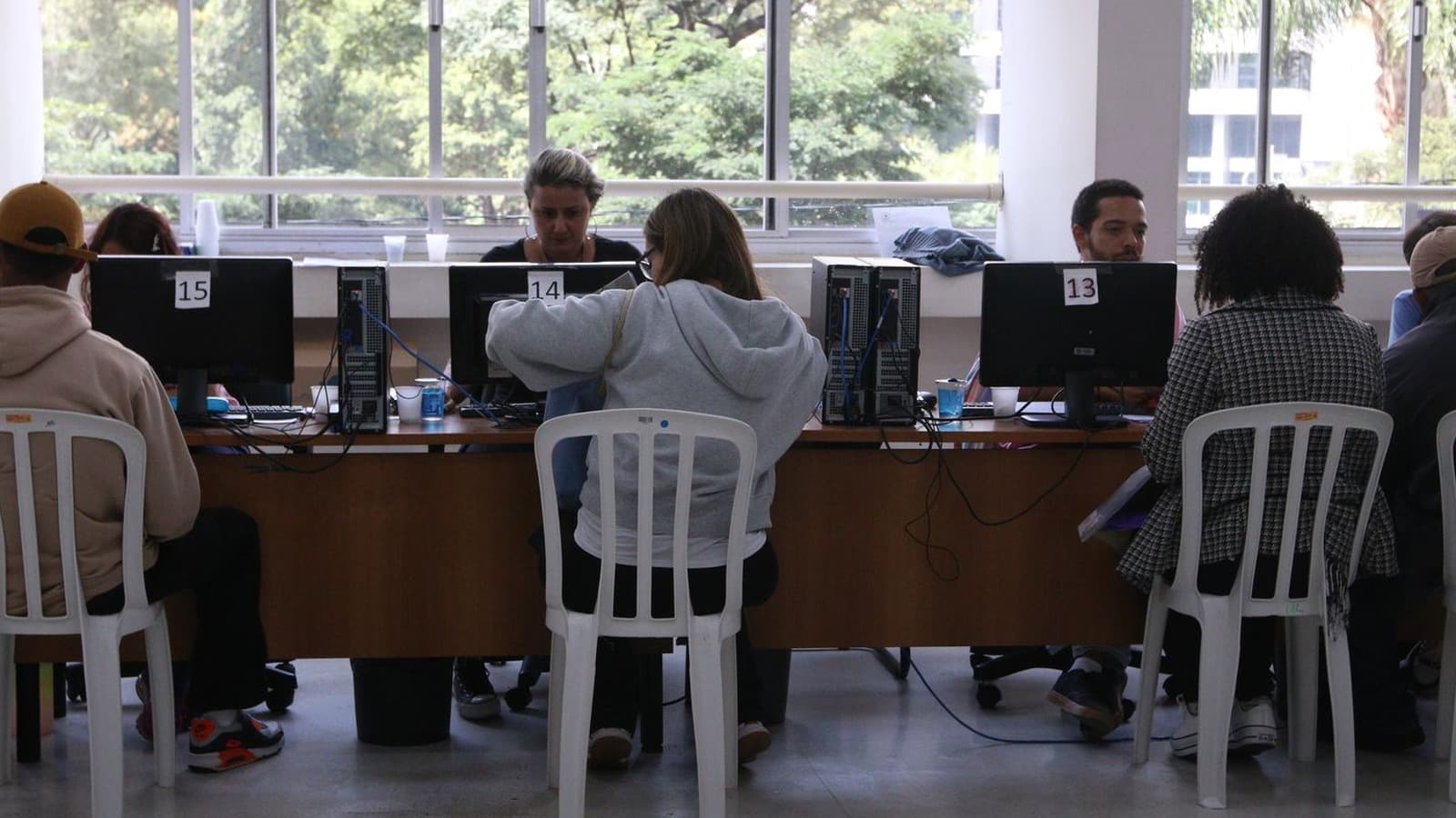 Consumidores sentados de costas são atendidos em guichês numerados com computadores durante mutirão de renegociação de dívidas; imagem de arquivo