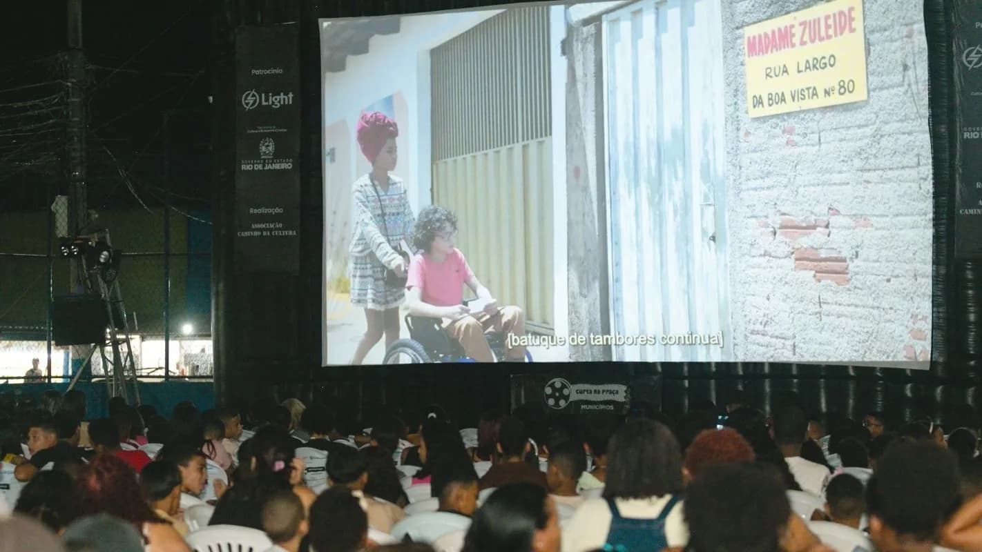 Público assiste a exibição de filme ao ar livre à noite, em sessão de cinema comunitário no Rio de Janeiro