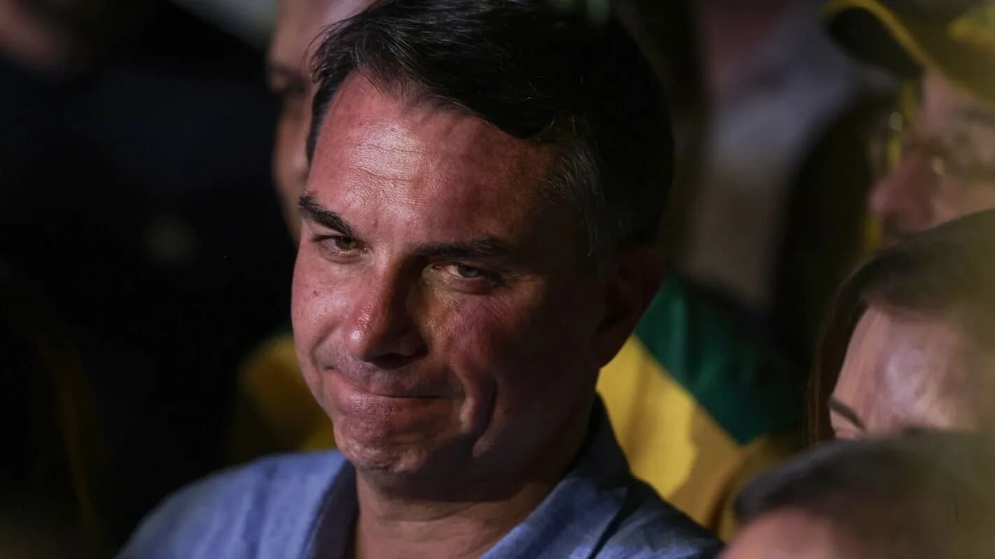 Flávio Bolsonaro em evento de campanha, com bandeira do Brasil ao fundo