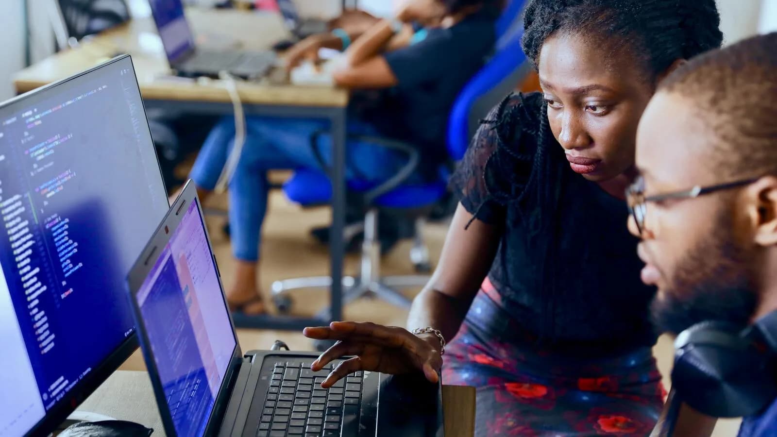 Duas pessoas olhando para tela de notebook com código de programação