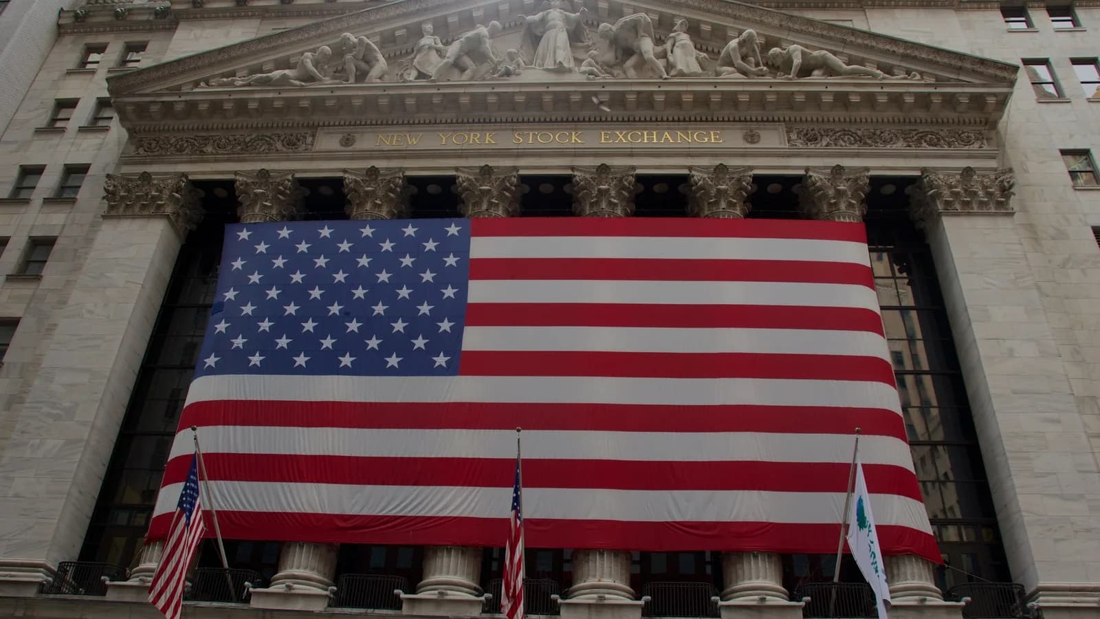 Fachada da Bolsa de Nova York (NYSE), em Wall Street, com uma grande bandeira dos Estados Unidos