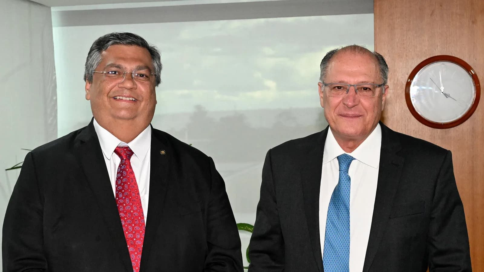 O ministro Flávio Dino sorrindo, de terno escuro e gravata vermelha