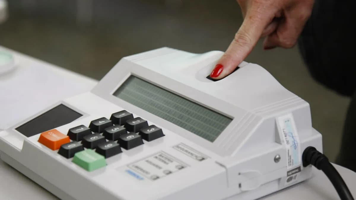 Mão com unha vermelha pressiona botão de urna eletrônica durante votação