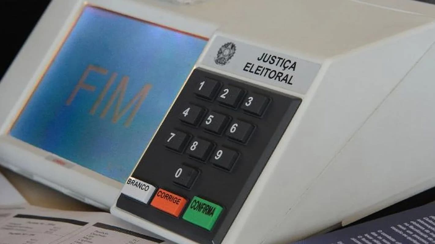 Urna eletrônica da Justiça Eleitoral exibindo a palavra FIM na tela, ao lado de material de votação