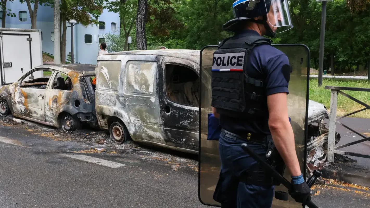 Policial ao lado de veículos incendiados durante protesto