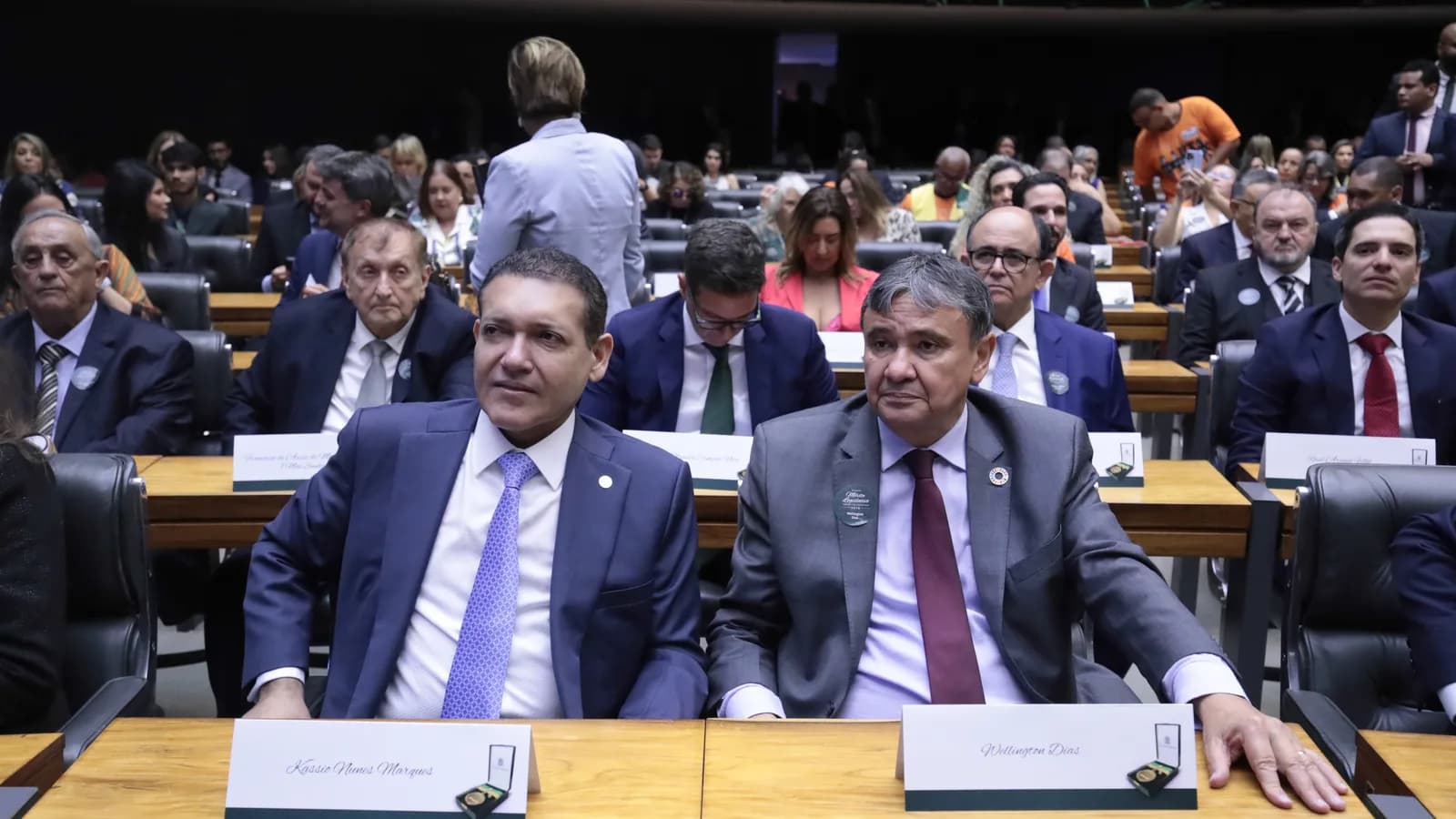 O ministro do TSE Kássio Nunes Marques sentado em plenário da Câmara dos Deputados, ao lado do senador Wellington Dias, durante cerimônia de dezembro de 2024