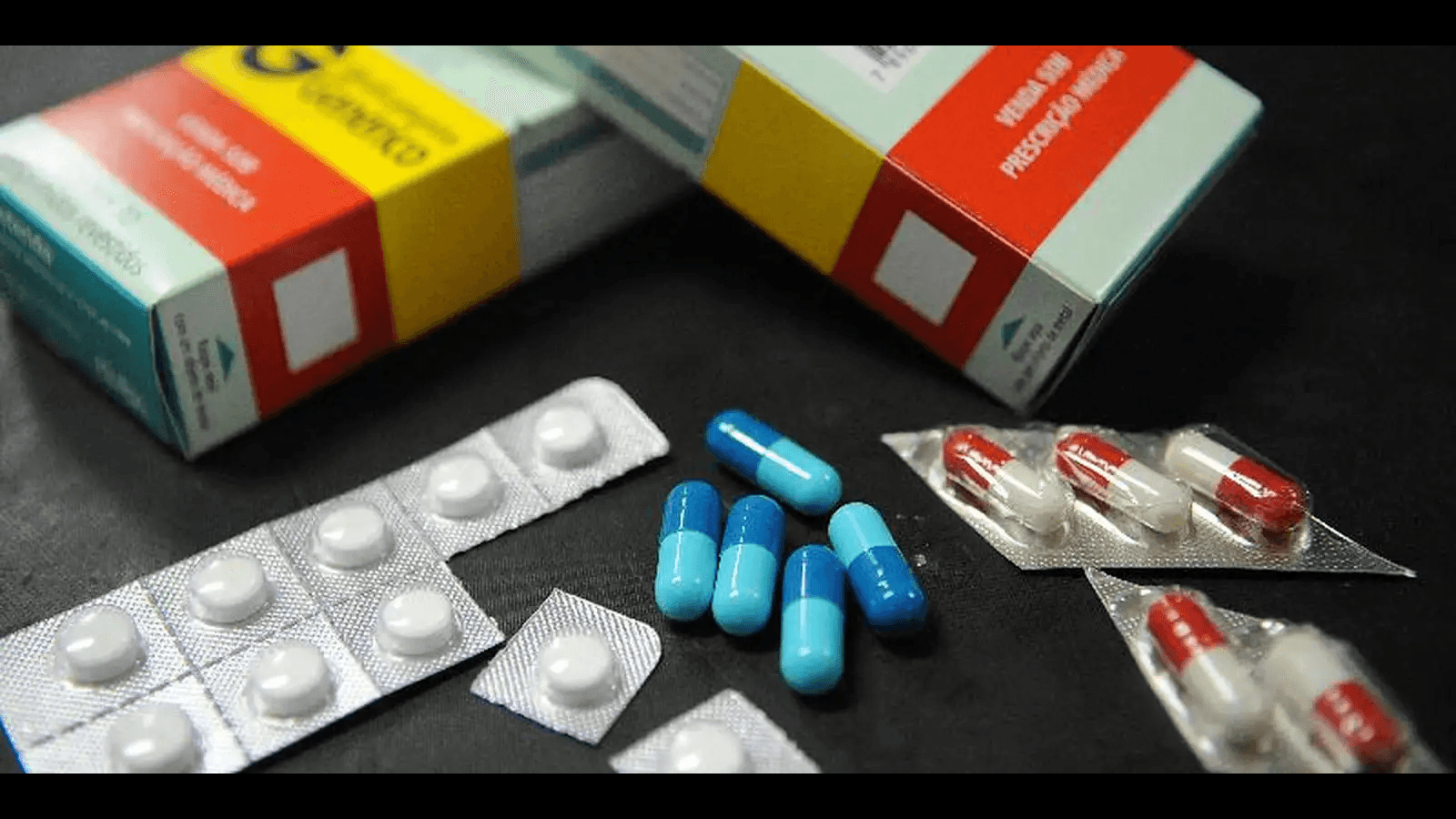 Caixas de remédios e cartelas de comprimidos e cápsulas sobre superfície escura, ilustrando medicamentos manipulados e industrializados