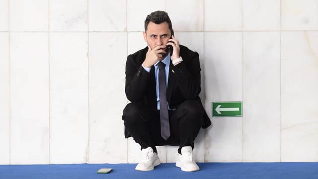 Foto de arquivo do senador Cleitinho, de terno preto e gravata, agachado ao lado de uma parede de mármore enquanto fala ao celular no Senado Federal