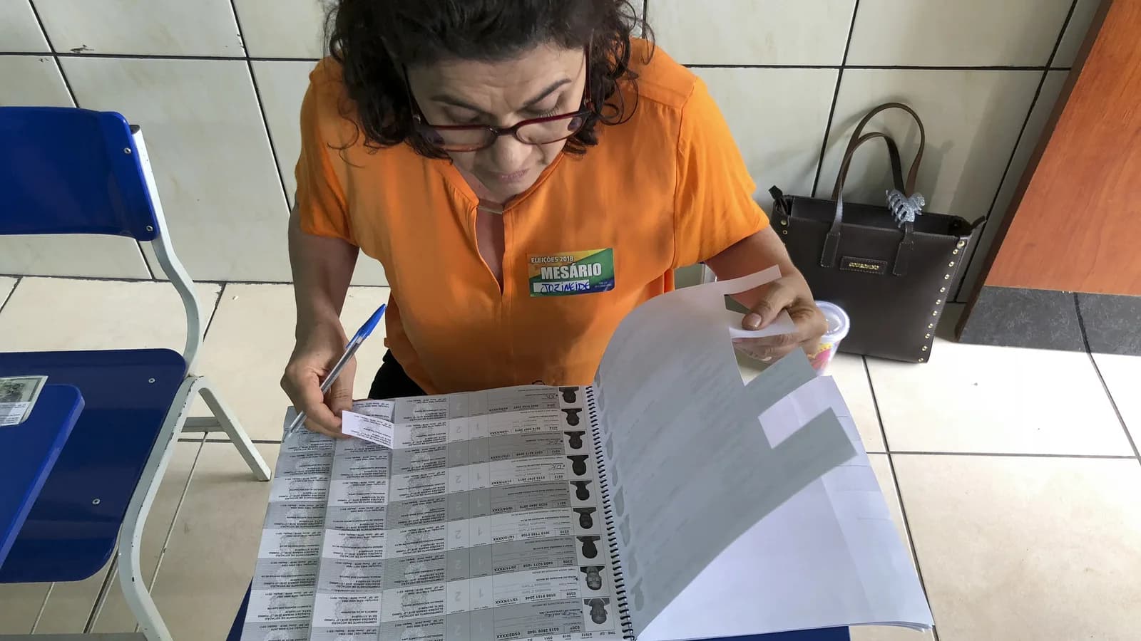 Mesária de uniforme laranja confere lista de eleitores em mesa de votação, em foto de arquivo de 2018