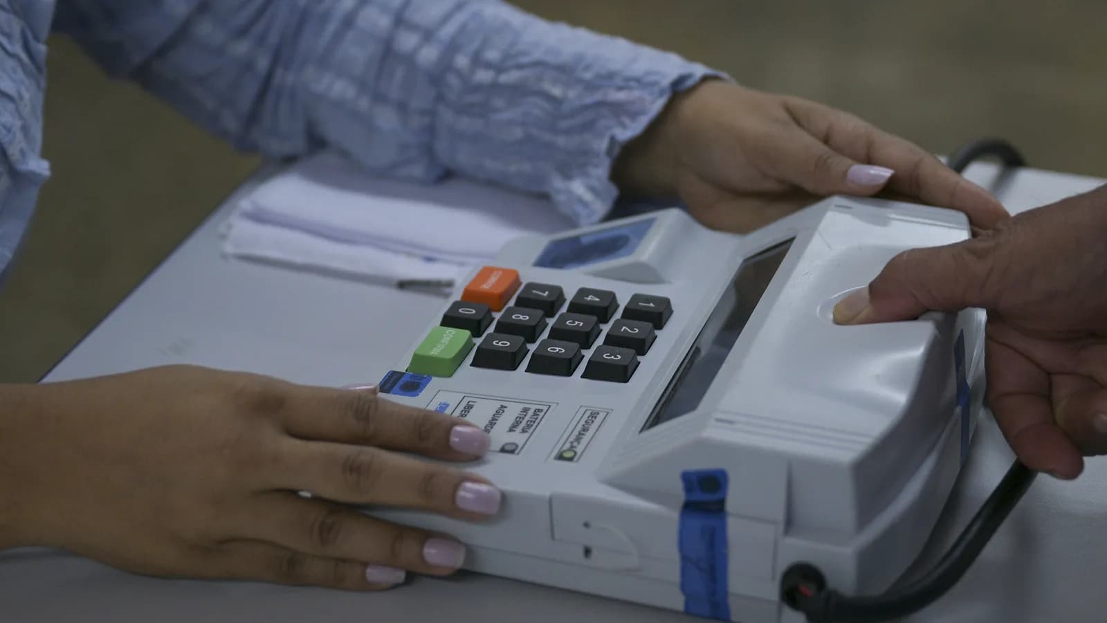 Mãos de eleitor e mesário em dispositivo de identificação biométrica durante o primeiro turno das Eleições 2026