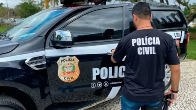 Agente da Polícia Civil ao lado de viatura, foto de arquivo ilustrativa