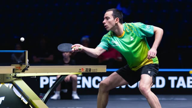 Hugo Calderano em ação durante partida de tênis de mesa, uniforme verde do Brasil
