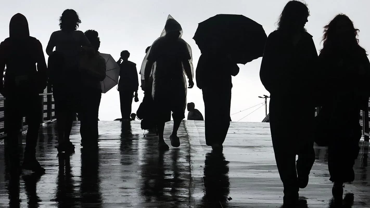 Pedestres caminham sob chuva em São Paulo, com guarda-chuvas, à noite