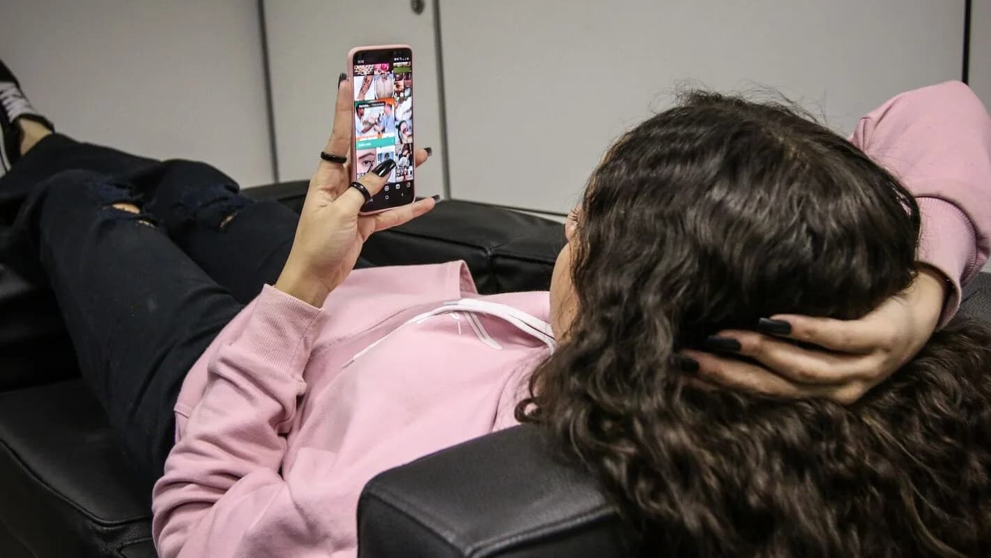 Adolescente reclinado no sofá usando smartphone