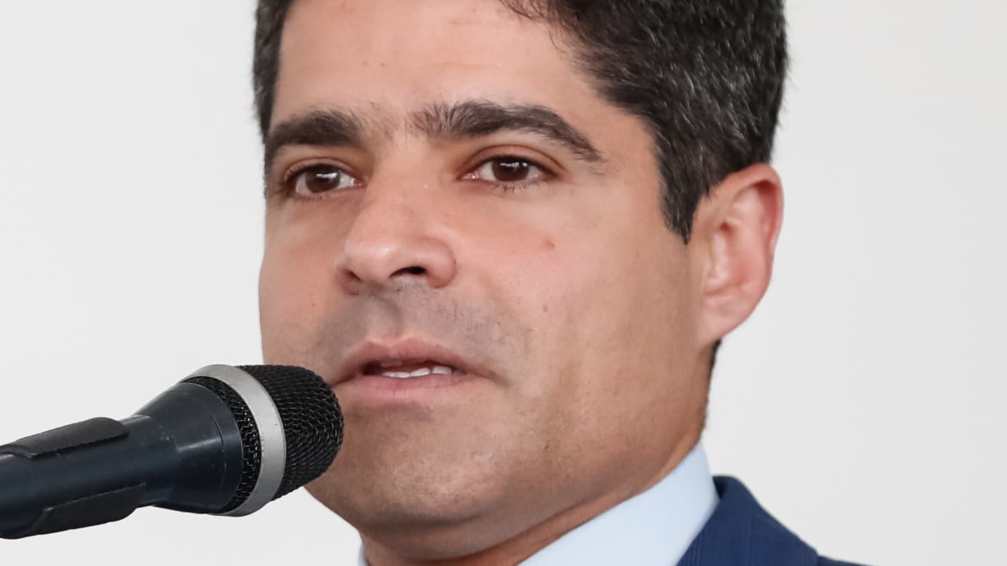 ACM Neto discursa ao microfone em cerimônia pública, de terno azul e gravata