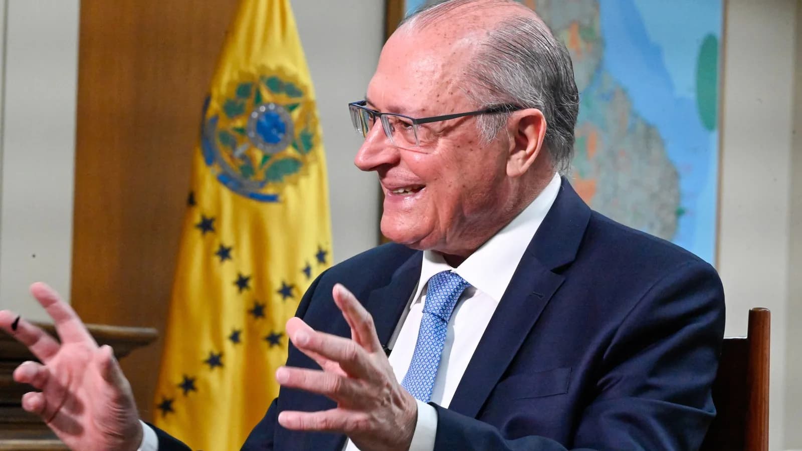 Geraldo Alckmin gesticula durante entrevista, em frente à bandeira do Brasil