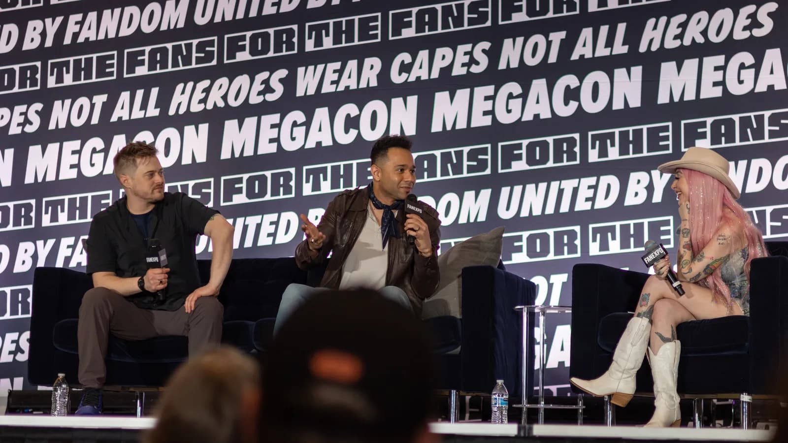 Corbin Bleu e Lucas Grabeel em painel de convenção geek, ambos sentados no palco com microfones