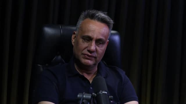 Rogério Furtado fala de forma pausada durante o podcast Encampus, em cadeira de couro preta contra fundo escuro