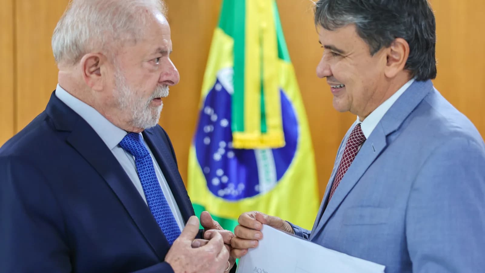 Lula conversa com o ministro do Combate à Fome, Wellington Dias, segurando documentos