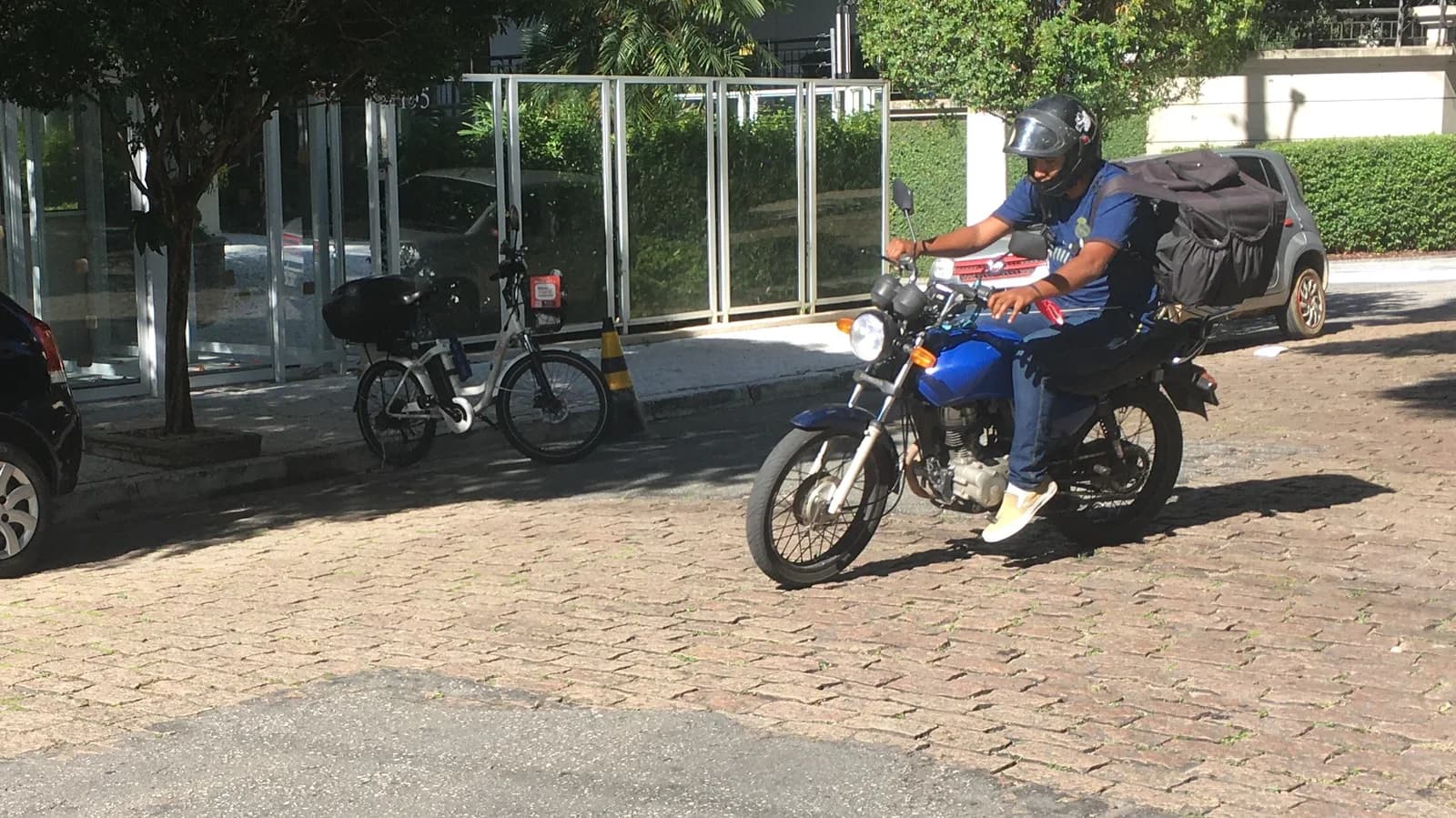 Entregador de aplicativo em motocicleta, com bolsa térmica de entrega, numa rua residencial