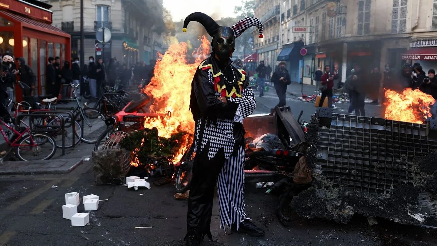 Barricada em chamas em rua de Paris durante protestos, com pessoas próximas ao fogo