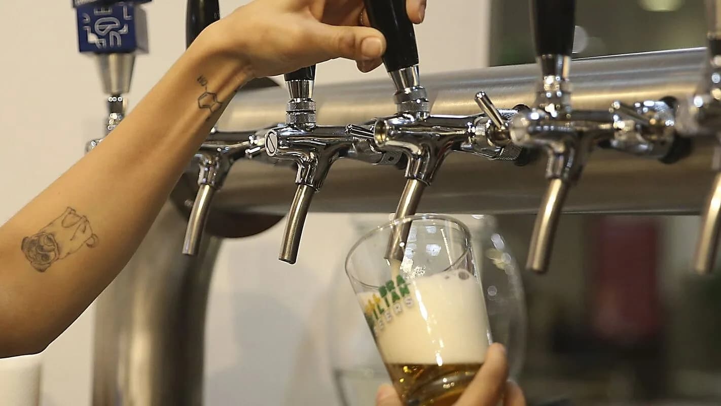 Mão servindo chope em copo de vidro em torneira de bar