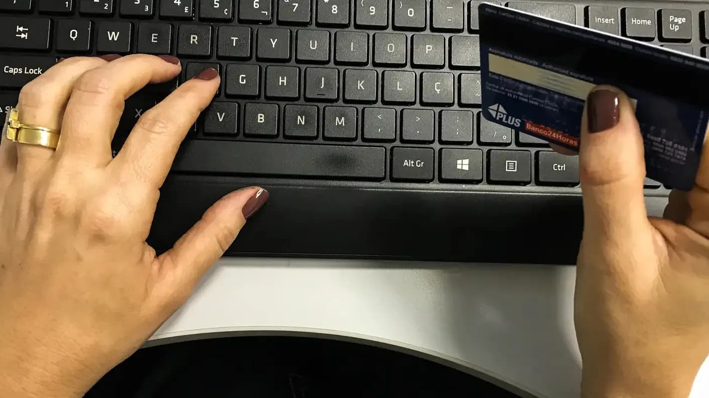 Mão de consumidor digita cartão de crédito em teclado de computador