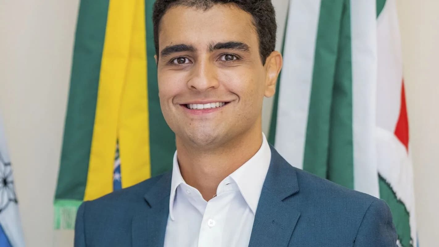JHC, candidato ao governo de Alagoas, sorri em retrato oficial com bandeiras ao fundo