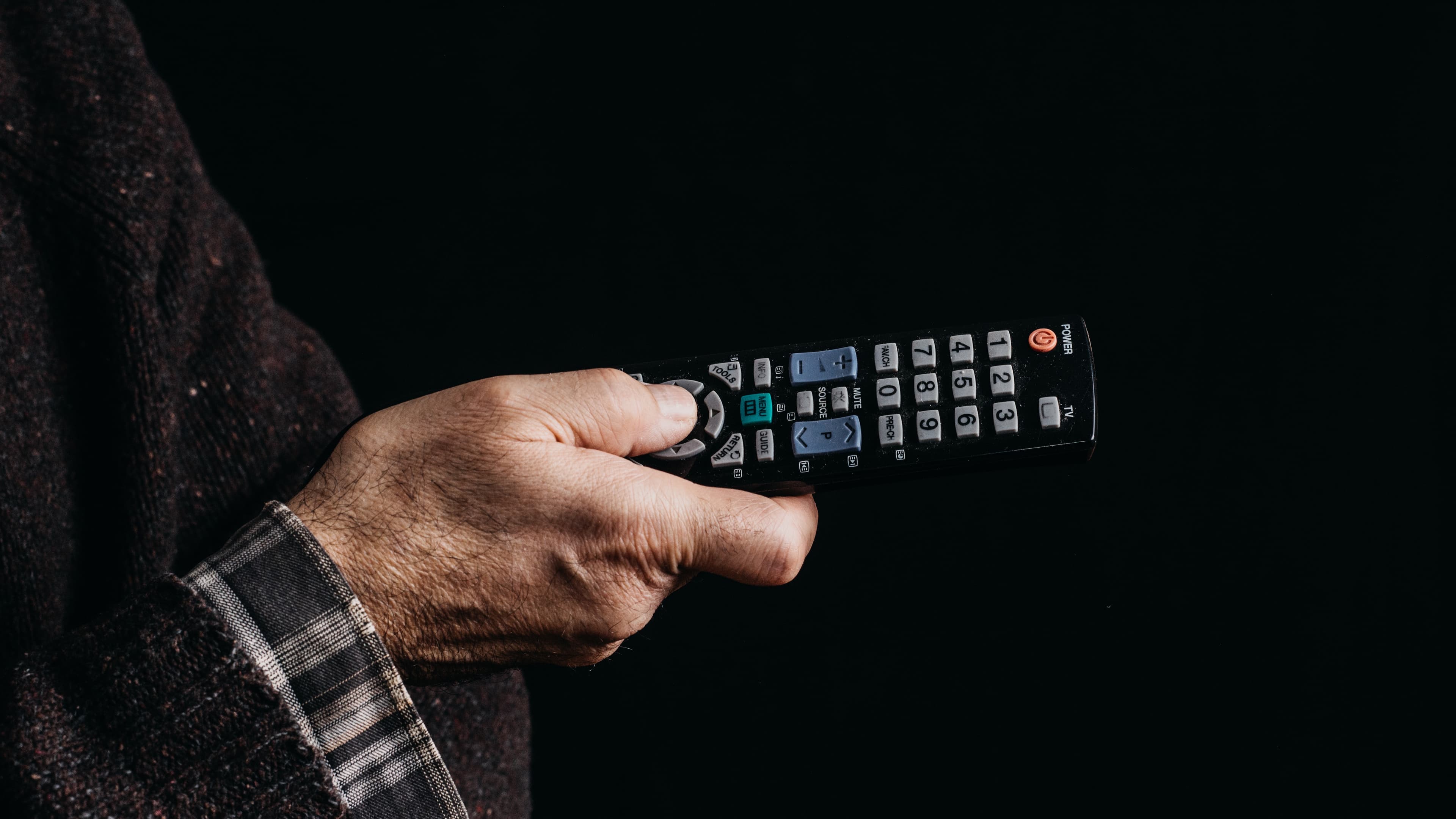 Mão segura um controle remoto de TV em ambiente escuro, prestes a escolher o que assistir