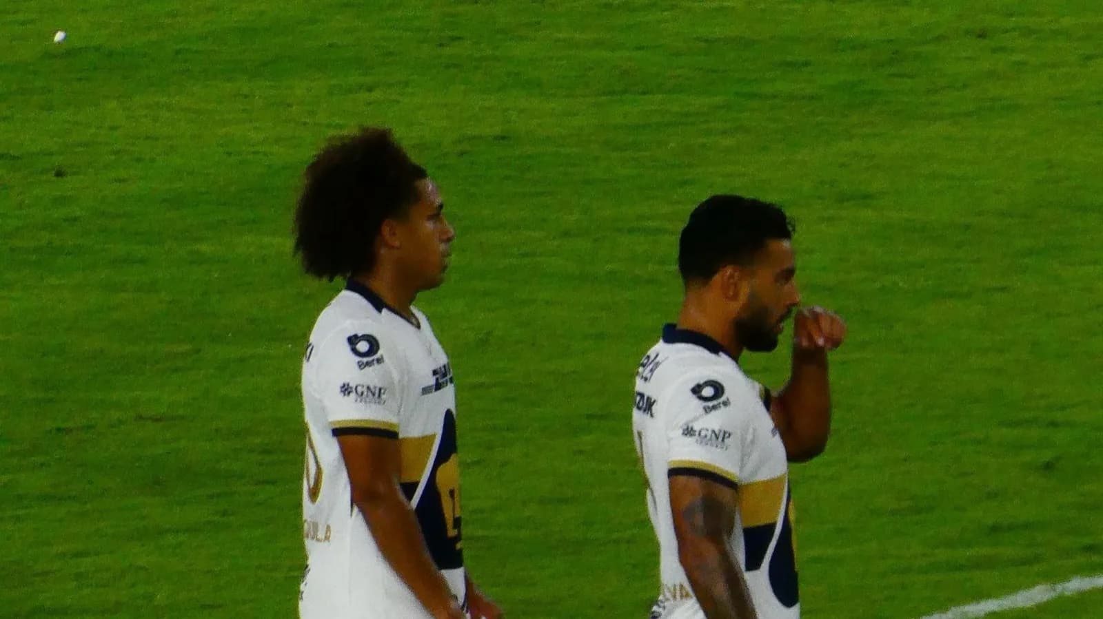 Dois jogadores do Pumas UNAM em campo com o uniforme branco e dourado do clube, em foto de arquivo