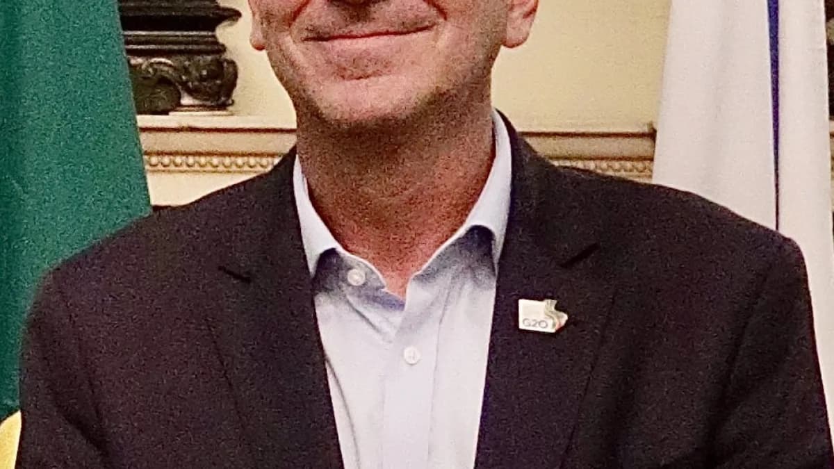 Eduardo Paes sorri em retrato oficial como prefeito do Rio de Janeiro, com bandeiras ao fundo