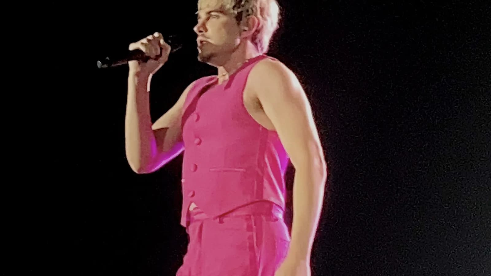 Jão se apresenta ao vivo, cantando ao microfone em show com figurino rosa