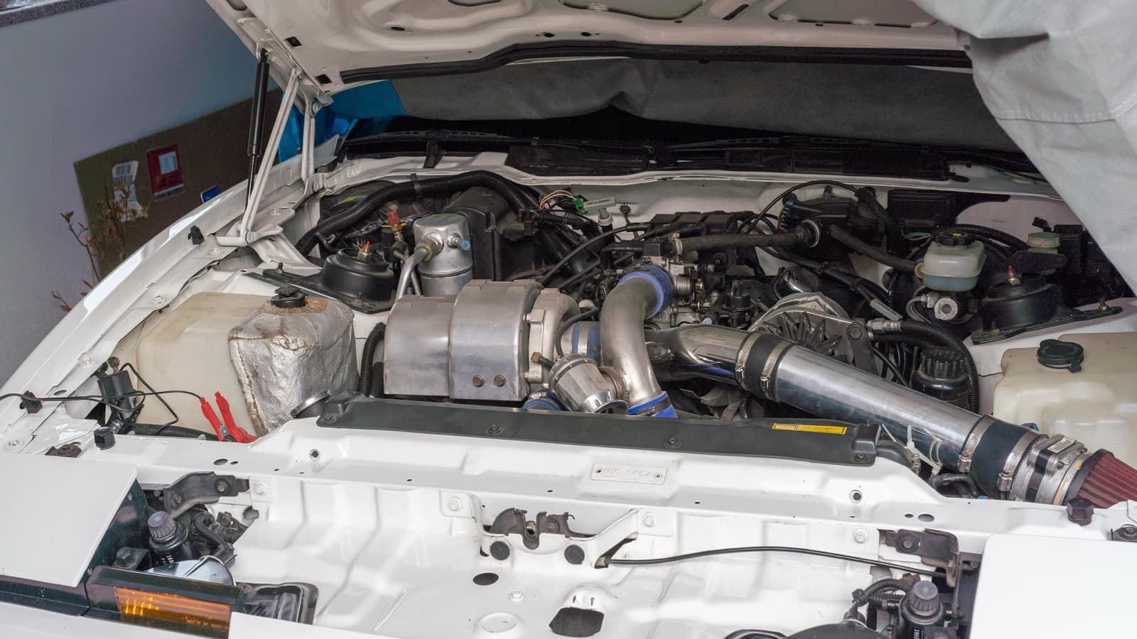 Cofre de motor aberto de um Pontiac Firebird Turbo Trans Am 1989 modificado, com dutos de admissão de alumínio e filtro de ar cônico à direita