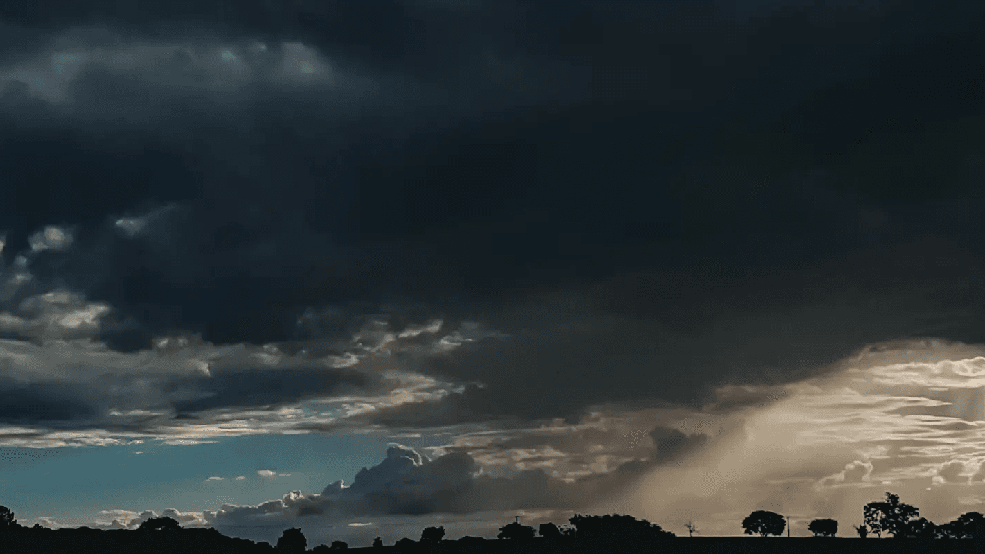 Céu tomado por nuvens escuras de tempestade ao entardecer, com feixes de luz entre as nuvens